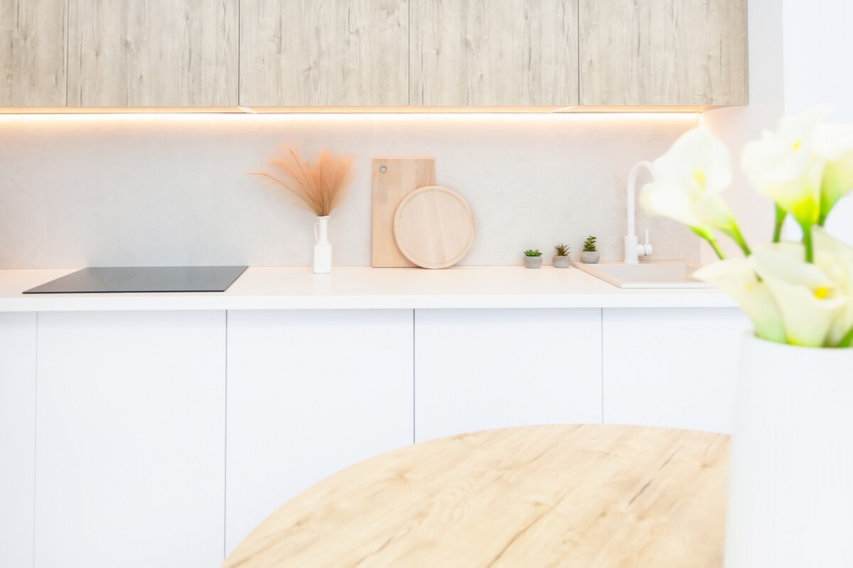 A modern kitchen with white cabinets, a white countertop, a wood countertop, and a sink. There are wooden cutting boards and a vase of flowers on the counter.